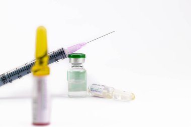 Beyaz yüzeye düşmüş bir ampul ve Coronavirus aşısı etiketini gösteren bir şişeye enjekte edilmiş.