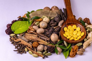 Ayurvedic tıp konsepti. Tahta kaşıkta Ayurvedic ilaçlar, çeşitli baharatlar ve beyaz arka planda yeşil yapraklar.
