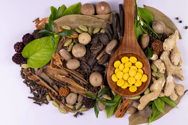 Ayurvedic tıp konsepti. Tahta kaşıkta bitkisel uyuşturucuların, dağınık baharatların ve beyaz arka planda yeşil yaprakların üst görüntüsü.