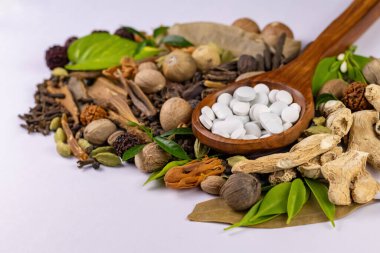 Beyaz tabletlerin yüksek açılı görüntüsü, arka planda kurutulmuş otlar ve beyaz yüzey var. Bitkisel ve Unani kavramı