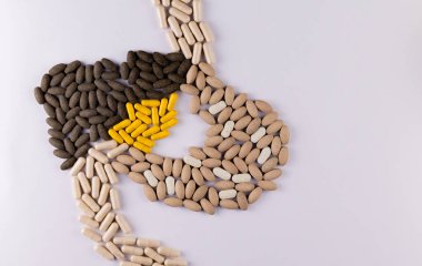 Safra kesesi gibi sarı kapsüller ve beyaz arka planda tabletlerden yapılmış karaciğer ve mide şekilleri. Karaciğer ilaçları konsepti