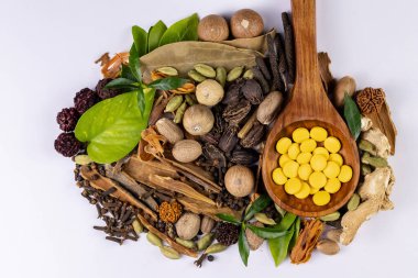 Geleneksel tıp konsepti. Tahta kaşıkta Ayurvedic ilaçlar, beyaz arka planda baharatlar ve yeşil yapraklar