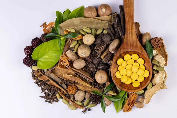 Geleneksel tıp konsepti. Tahta kaşıkta Ayurvedic ilaçlar, beyaz arka planda baharatlar ve yeşil yapraklar