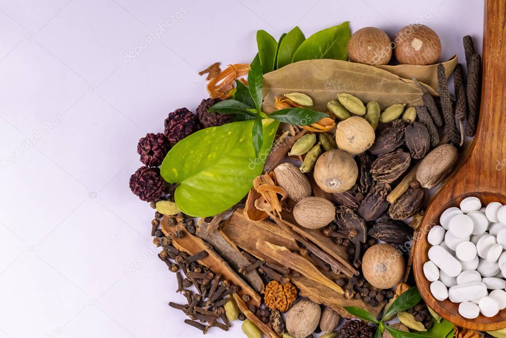 Top view of assorted Indian Spices with green leaves and white herbal tablets in a wooden spoon. herbal concept