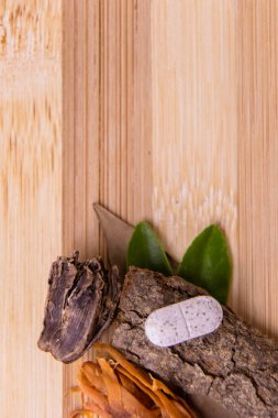 Tek bir beyaz tablet ahşap bir kabuğa yerleştirilmiş yeşil yapraklar ve baharatlar ahşap arka planda. Doğal kavrayış