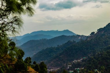 Ağaçlarla kaplı dağların dramatik fotoğrafları ve arka planda bulutlu gökyüzü