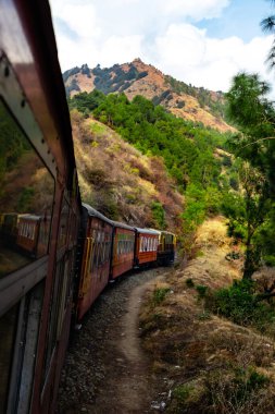 tren arka planda bulutlu gökyüzü ve ağaçlar boyunca yol almaktadır.