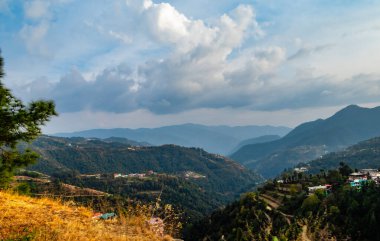 Tepede küçük bir ev, tepenin üstünde yol ve dağların arkasında bulutlu mavi gökyüzü, doğa konsepti.