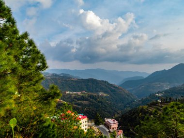 Bulutlu mavi gökyüzünün altında ağaçlarla çevrili dağların inanılmaz fotoğrafları.