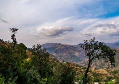 Bulutlu mavi gökyüzü ve ön planda ağaçlar olan dağların güzel manzarası