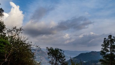 Dağların ve ağaçların arkasındaki güzel bulutlu gökyüzünün geniş bir görüntüsü.