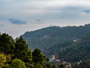 Önünde ağaçlar ve arka planında bulutlu gökyüzü olan güzel tepelerin geniş bir görüntüsü, doğa konsepti.