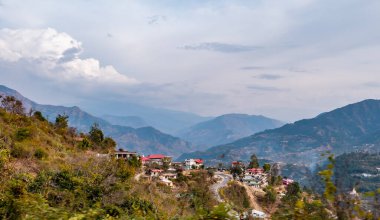 Güzel dağların geniş bir görüntüsü ve bulutlu gökyüzünün altında küçük bir kasaba.