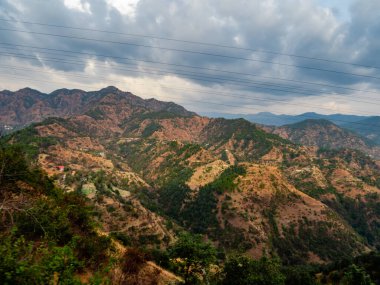 Bulutlu bir günde dağların geniş bir görüntüsü ve güneş ışığı kayalıklara düşüyor, gerisini gölgeler içinde bırakıyor.