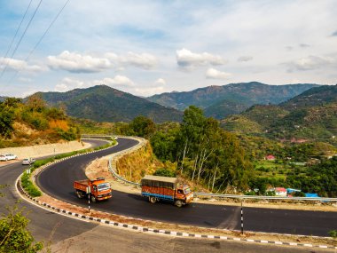 Tepeler boyunca giden kamyonların geniş açılı görüntüsü ve arka planda bulutlar, ulaşım konsepti