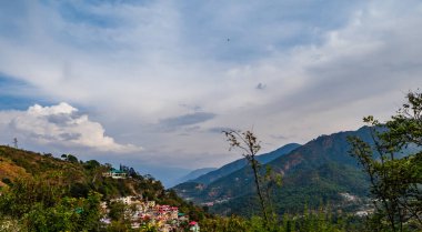 Tepelerin geniş manzarası ve bulutlu mavi gökyüzü. Önünde güzel bir vadi, doğa ve güzellik kavramı var.