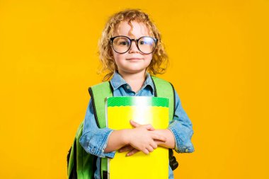 Sırt çantalı, kıvırcık saçlı Avrupalı bir kız stüdyoda sarı bir arka planda duruyor.