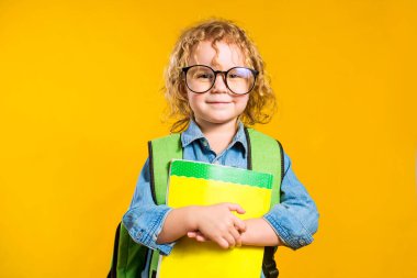 Sırt çantalı, kıvırcık saçlı Avrupalı bir kız stüdyoda sarı bir arka planda duruyor.