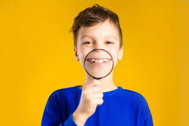 Stüdyoda sarı arka planda büyüteç takan bir çocuk, koca ağızlı bir portre.