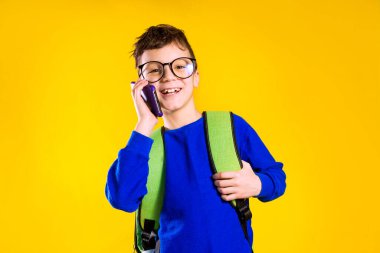 Stüdyoda sarı arka planda sırt çantası ve telefonu olan okul çocuğu.