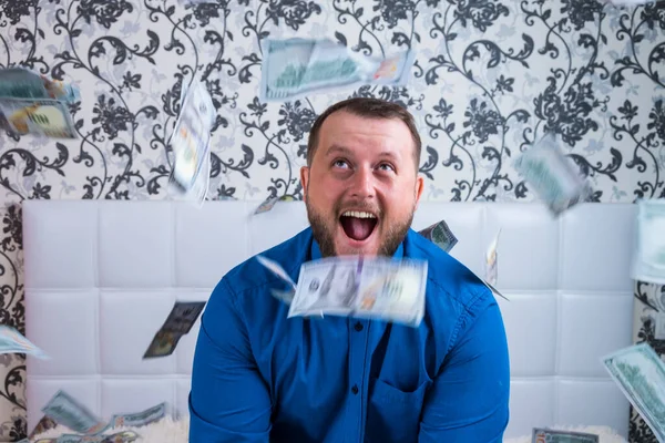 A nice man with a beard in a blue shirt, rejoices at the dollars, throws them up and counts. Win lottery — Stock Photo, Image