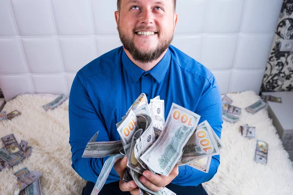A nice man with a beard in a blue shirt, rejoices at the dollars, throws them up and counts. Win lottery — Stock Photo, Image