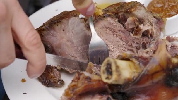 男人用手和叉子割下猪肉的拐杖，放在盘子里。附近是一杯啤酒. — 图库视频影像