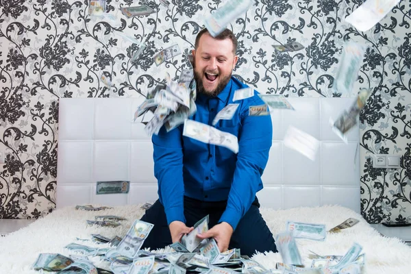 A nice man with a beard in a blue shirt, rejoices at the dollars, throws them up and counts. Win lottery — Stock Photo, Image