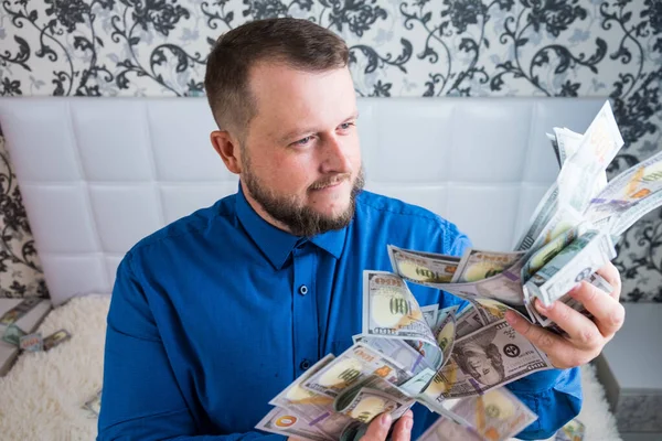 Ένας καλός άντρας με μούσι σε μπλε πουκάμισο, χαίρεται με τα δολάρια, τα πετάει και μετράει. Κερδίστε κλήρωση — Φωτογραφία Αρχείου