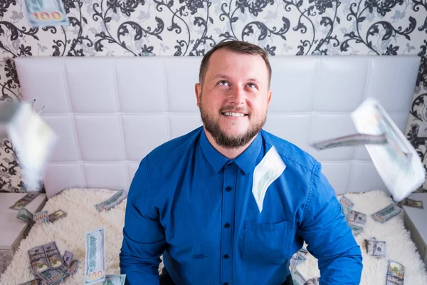 A nice man with a beard in a blue shirt, rejoices at the dollars, throws them up and counts. Win lottery — Stock Photo, Image