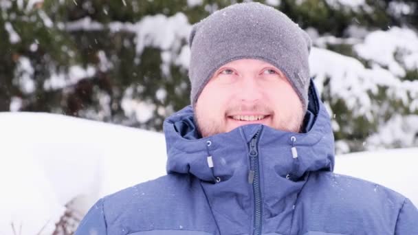 Een man met een baard geniet van de vallende sneeuw op een winterdag. — Stockvideo