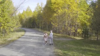 Kadın ve bir erkek, sonbahar ormanlarında asfalt bir yolda yürür ve koşarlar.
