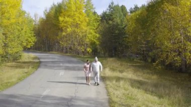 Kadın ve bir erkek, sonbahar ormanlarında asfalt bir yolda yürür ve koşarlar.