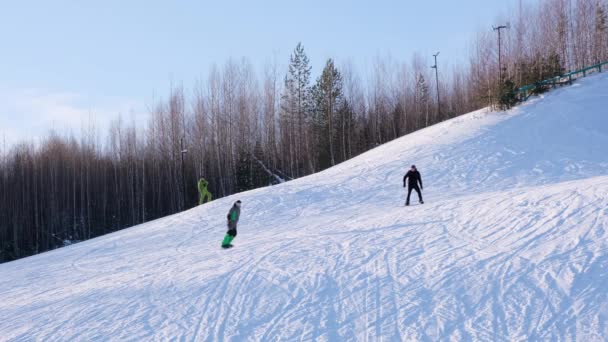 Esquiadores y snowboarders montando en una estación de esquí en una montaña nevada de invierno con vista panorámica de fondo — Vídeos de Stock