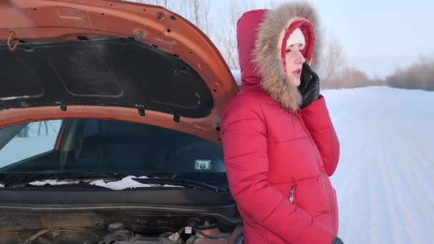 Дівчина в червоному зимовому костюмі стоїть поруч з розбитою машиною і плаче . — стокове відео