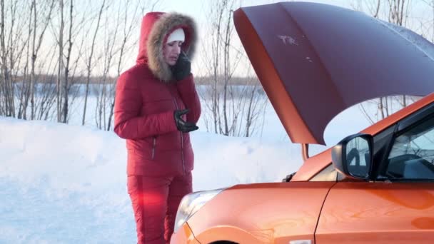 Девушка в красном зимнем красном костюме стоит рядом со сломанной машиной . — стоковое видео