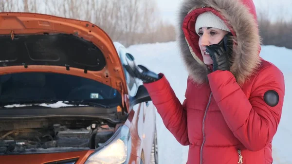 A girl in a red winter suit stands next to a broken car and crying.