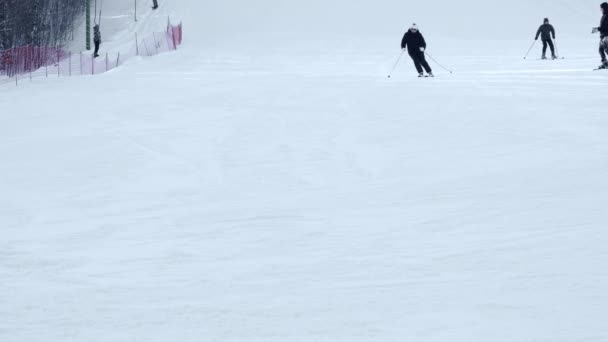 Esquiadores y snowboarders montando en una estación de esquí en una montaña nevada de invierno con vista panorámica de fondo — Vídeo de stock