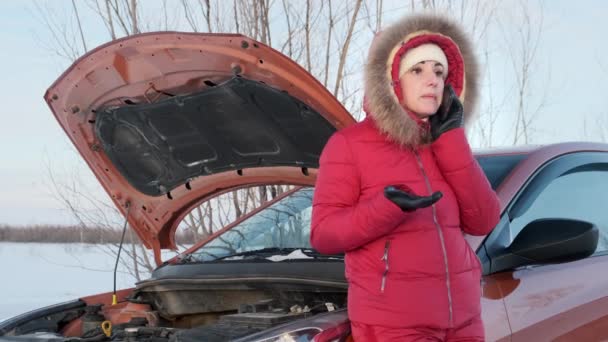 Una chica con un traje rojo de invierno está al lado de un coche roto y llorando . — Vídeo de stock