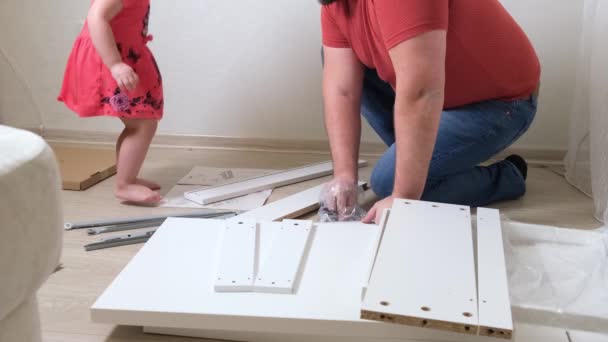 Dad and daughter collect furniture in the living room of the house together. Daughter will help dad. — Stock Video