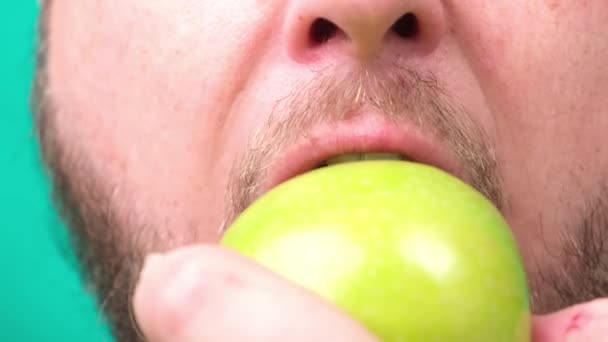 Een dikke man met een baard eet een groene appel. Close-up — Stockvideo