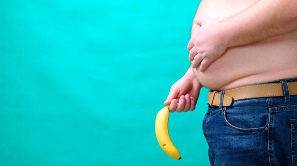 A man with a large belly holds a banana lowered to the bottom of. male sexuality, man sex and relationship problem concept