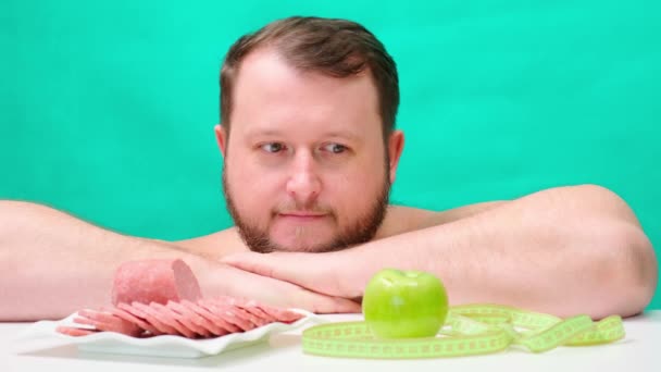 Товстий, пухкий чоловік з бородою зробив вибір на користь ковбаси і здорового способу життя замість зеленого яблука і краси — стокове відео