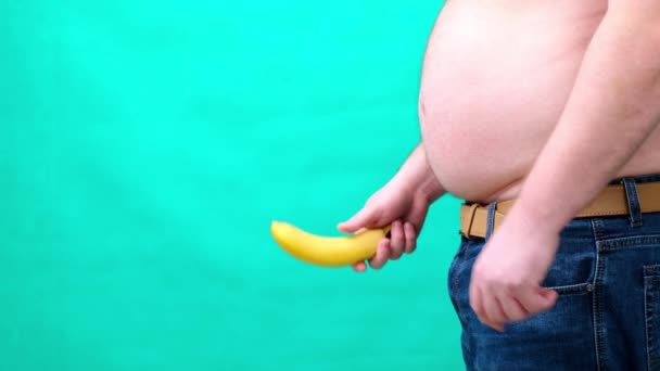 Een man met een grote buik houdt een banaan op de bodem van. mannelijke seksualiteit, man geslacht en relatie probleem concept — Stockvideo