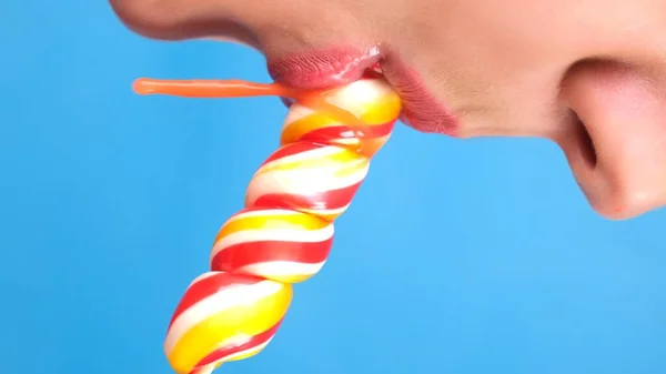 Verticale close-up, vrouwelijke sexy lippen met rode lippenstift zuigen grote spiraalvormige langwerpige snoeplolly. kopieer ruimte. blauwe achtergrond — Stockfoto