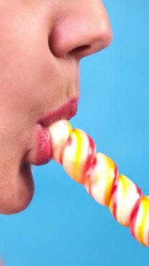  dikey yakın plan, kırmızı rujlu seksi dudaklar büyük sarmal şeker lolipopu emer. kopyalama alanı. mavi arkaplan 