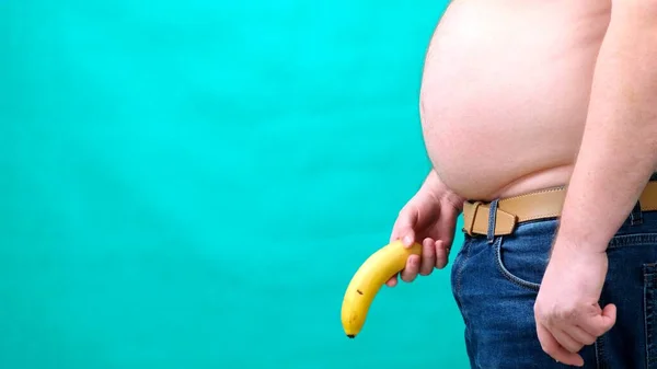 Een man met een grote buik houdt een banaan op de bodem van. mannelijke seksualiteit, man geslacht en relatie probleem concept — Stockfoto