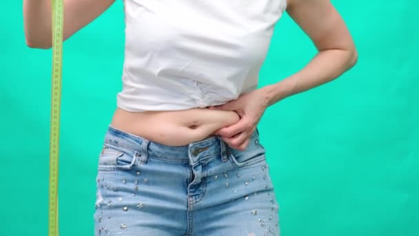 Une femme sur fond de ruban à mesurer et de pomme verte, touche et mesure son estomac gras, contrôle du poids corporel, vêtements autour de l'abdomen — Video