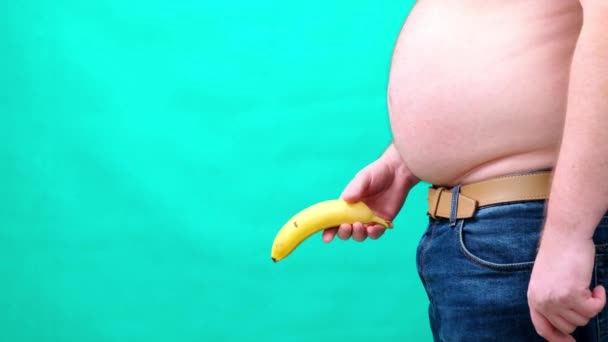 Een man met een grote buik houdt een banaan op de bodem van. mannelijke seksualiteit, man geslacht en relatie probleem concept — Stockvideo