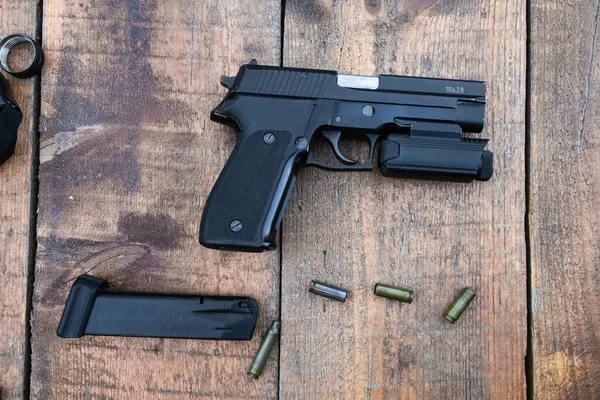 Pistol with included tactical lantern lies on a wooden table, next to lies clip and bullets — Stock Photo, Image